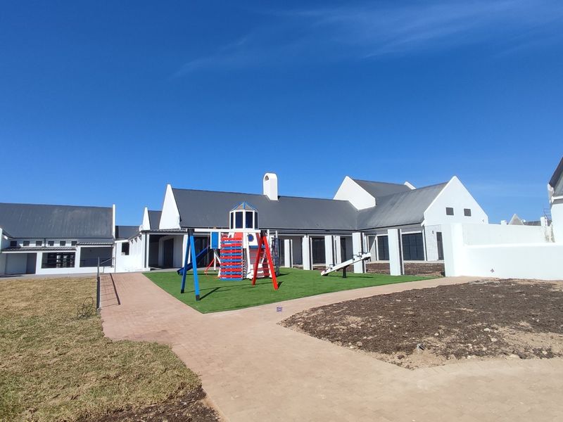 Rear view of the property featuring a paved walkway, artificial lawn area, and white exterior walls under a clear blue sky.
