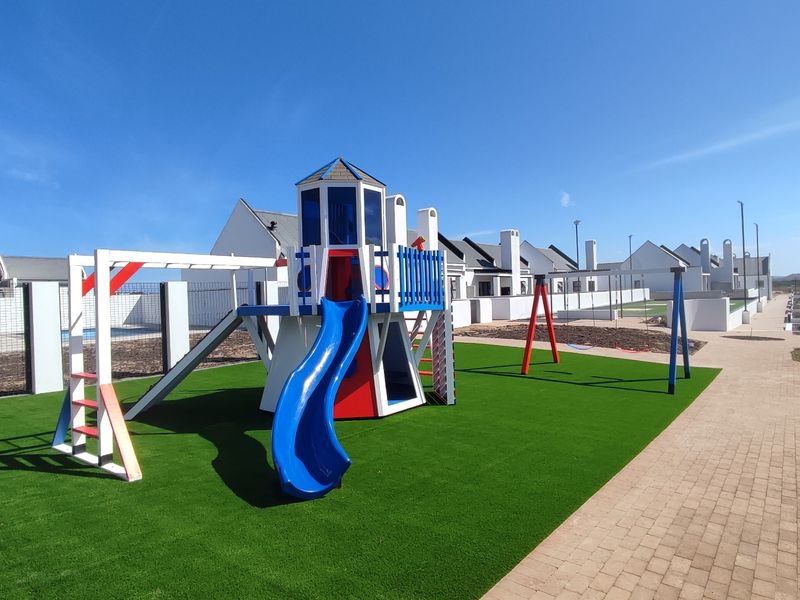 A well-maintained communal garden area featuring artificial turf, a children's playground structure, and paved walkways within a residential estate.