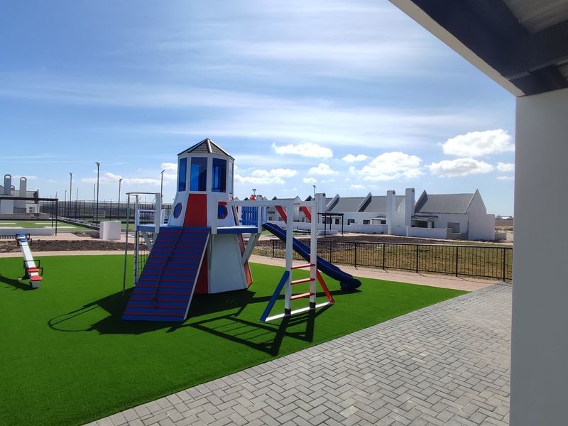 A well-maintained outdoor communal garden area featuring artificial turf, a paved walkway, and a children's playground structure within a residential estate.