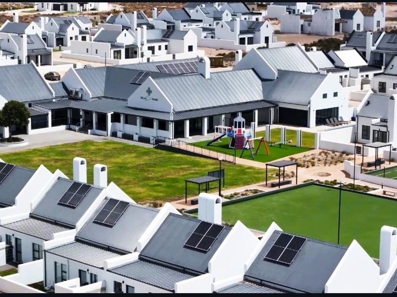 Aerial view of a modern residential estate featuring uniform white houses with grey metal roofs, solar panels, and communal recreational facilities.
