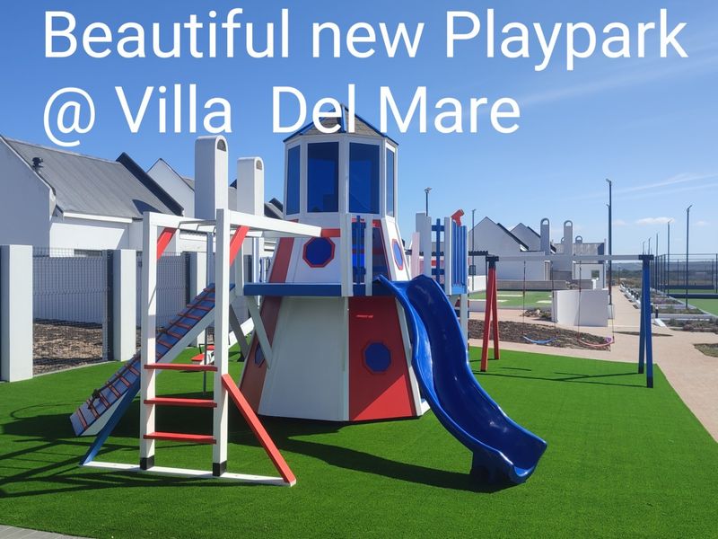 A well-maintained communal play area featuring modern playground equipment, artificial turf, and paved pathways within a residential estate.