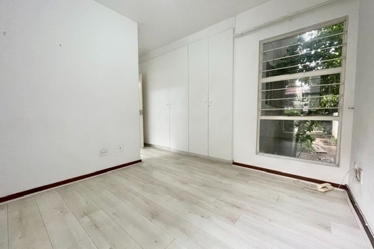 An empty bedroom featuring light-toned laminate flooring, built-in cupboards, and a window fitted with security bars.