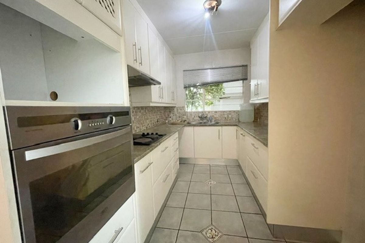 A functional galley-style kitchen featuring white cabinetry, built-in oven, hob, extractor fan, and tiled flooring with a mosaic backsplash.