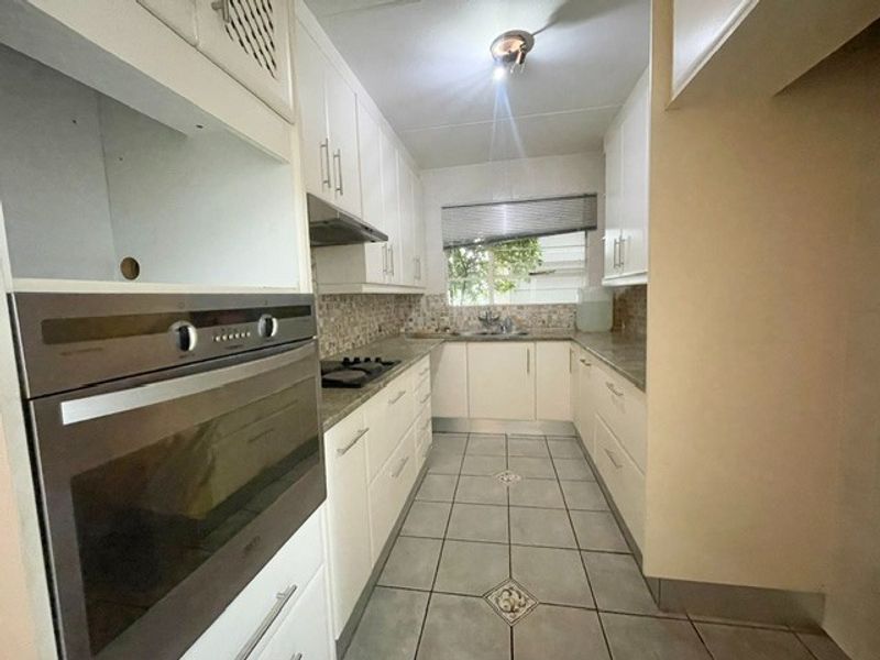 A functional galley-style kitchen featuring white cabinetry, built-in oven, hob, extractor fan, and tiled flooring with a mosaic backsplash.