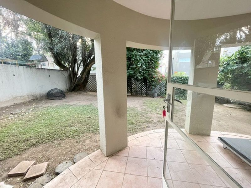 A covered patio area featuring tiled flooring and concrete pillars, providing direct access to a private garden space with boundary walls.