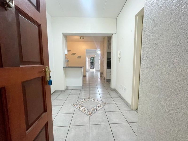 An entrance hallway featuring tiled flooring with a decorative inlay, leading into an open-plan living and kitchen area.