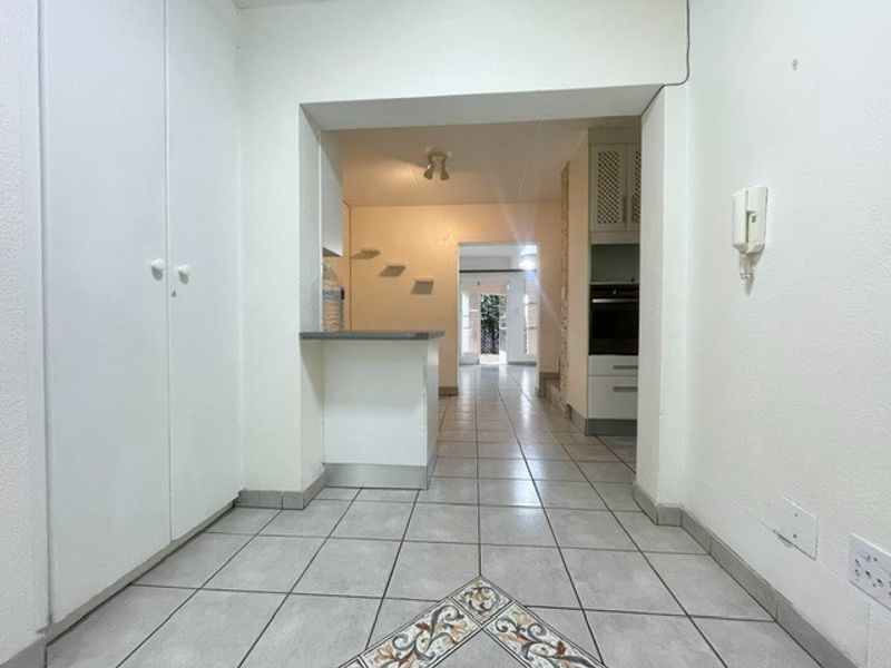 An open-plan apartment interior featuring tiled flooring, built-in cabinetry, and a breakfast counter, leading through to a kitchen area.