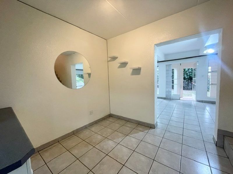 An open-plan living area featuring neutral tiled flooring, built-in wall shelving, and direct access to an outdoor space through glass panel doors.