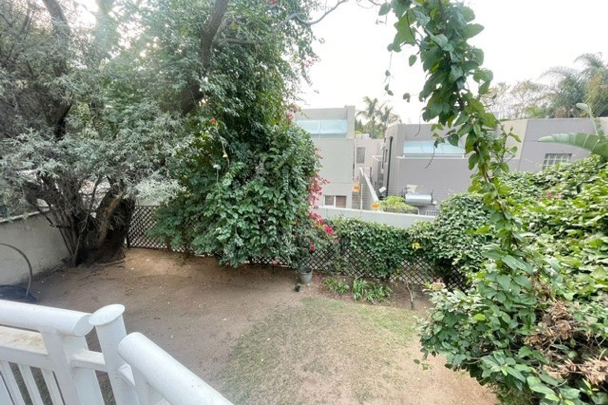 A view of the rear garden area featuring a white railing, boundary wall, and established garden greenery.