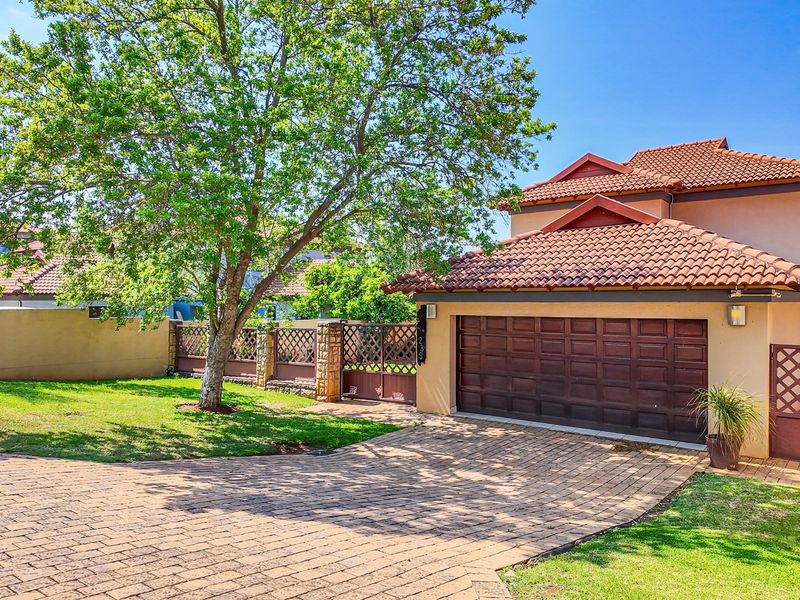 Front elevation of a double-story house featuring a paved driveway, double garage, and established garden with boundary wall and gate.