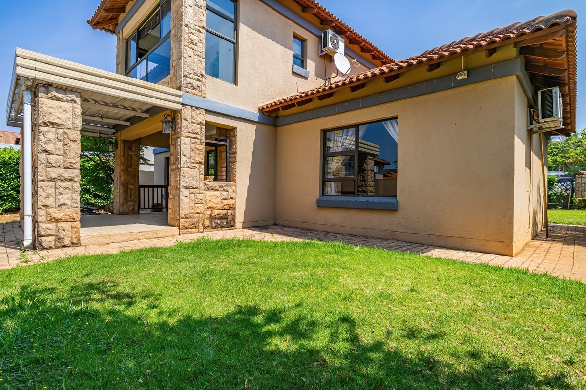 Rear view of the property featuring a covered patio, stone-clad pillars, tiled roof, and a well-maintained lawn area.