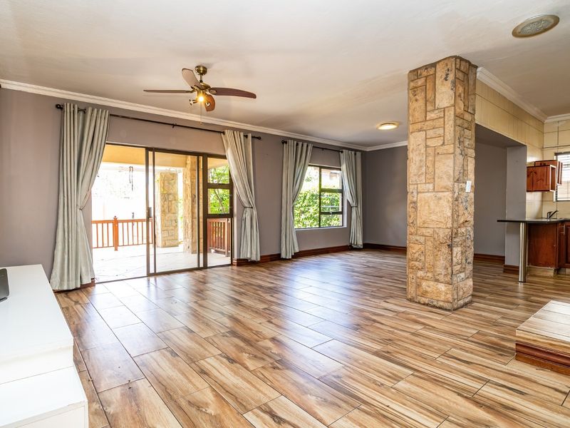 Spacious open-plan living area featuring wood-look tile flooring, a distinctive stone-clad pillar, and direct access to an outdoor patio through sliding glass doors.