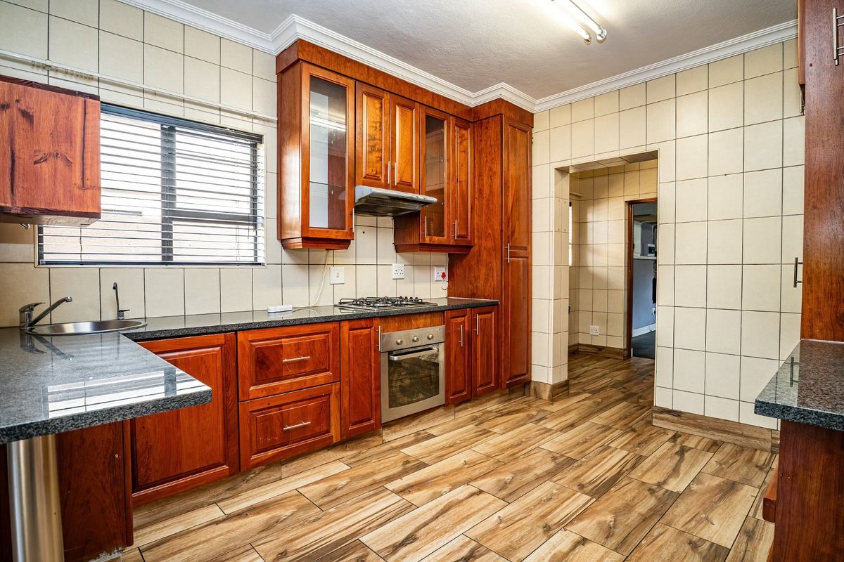 A well-maintained kitchen featuring warm-toned wooden cabinetry, granite countertops, a gas hob, built-in oven, and durable wood-look floor tiles.