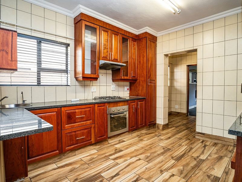 A well-maintained kitchen featuring warm-toned wooden cabinetry, granite countertops, a gas hob, built-in oven, and durable wood-look floor tiles.