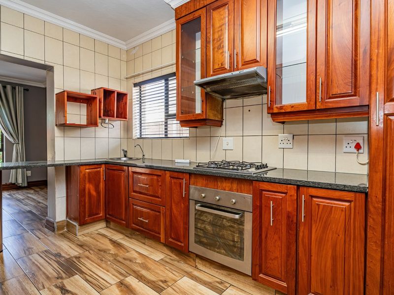 Functional kitchen featuring warm-toned wooden cabinetry, granite countertops, a gas hob, built-in oven, and durable wood-look floor tiles.