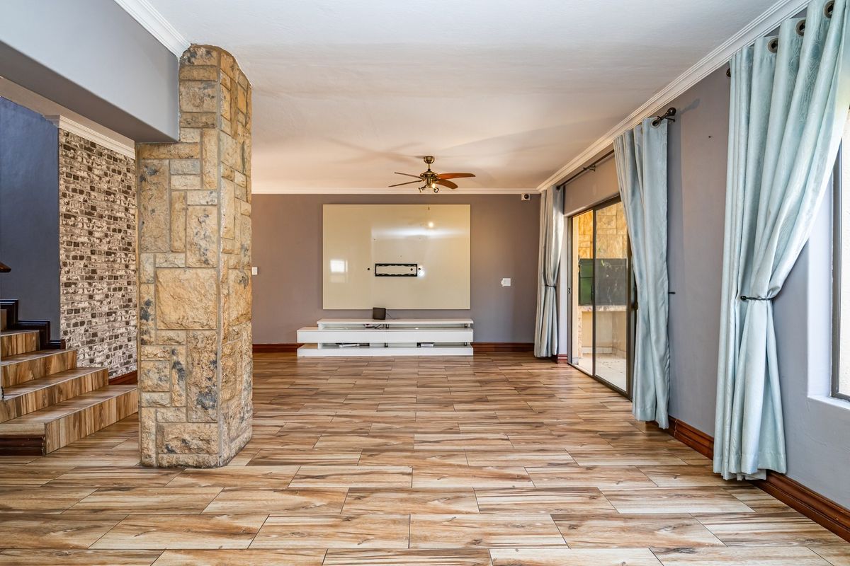 Spacious living area featuring wood-look tile flooring, a prominent stone-clad pillar, brick-veneer accent wall, and sliding glass doors leading to the exterior.