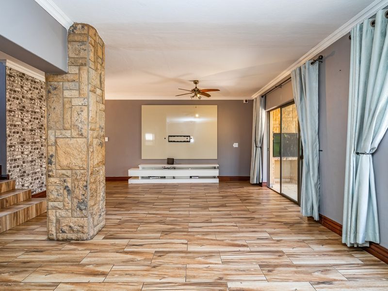 Spacious living area featuring wood-look tile flooring, a prominent stone-clad pillar, brick-veneer accent wall, and sliding glass doors leading to the exterior.