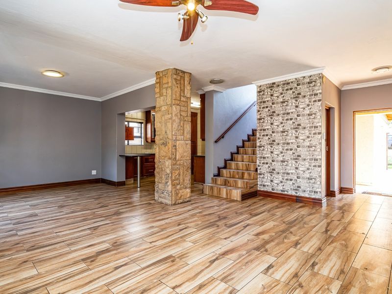 Spacious open-plan living area featuring wood-look tile flooring, a decorative stone-clad pillar, a brick-effect feature wall, and a staircase leading to the upper level.