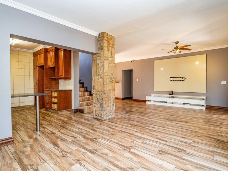 Spacious open-plan living area featuring a distinctive stone-clad pillar, wood-toned cabinetry, and modern wood-look tiled flooring throughout.