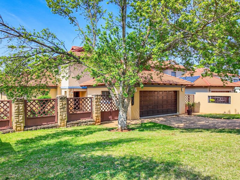 Front view of a residential property featuring a tiled roof, paved driveway, integrated garage, and stone-accented boundary wall with metal fencing.