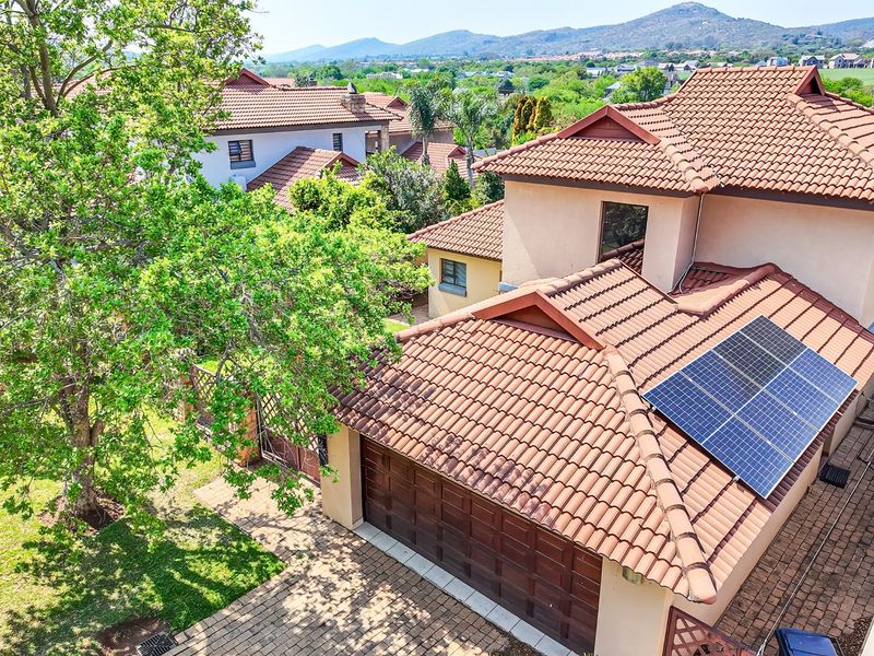 Aerial view of the property featuring a tiled roof with integrated solar panels, a paved driveway, and a well-maintained garden.