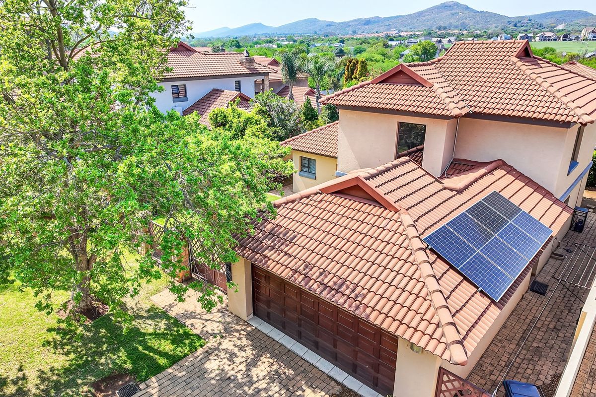 Aerial view of the property featuring a tiled roof with integrated solar panels, a paved driveway, and a well-maintained garden.
