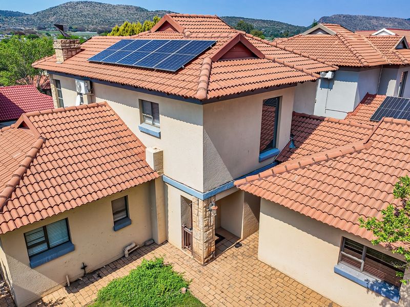 Aerial view of the property featuring a tiled roof with integrated solar panels and a paved courtyard area.