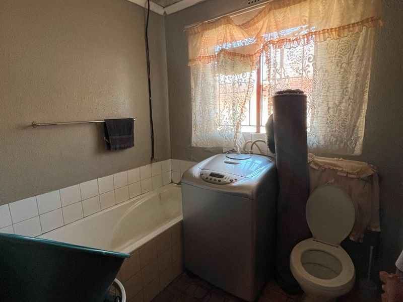 A functional bathroom featuring a built-in bathtub, toilet, and tiled flooring, with decorative ceiling tiles and a window providing natural light.