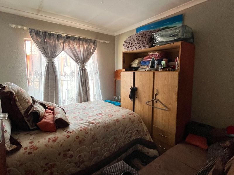 A compact bedroom featuring a window with curtain rods and a ceiling light fixture, requiring some cosmetic updates to the ceiling and walls.