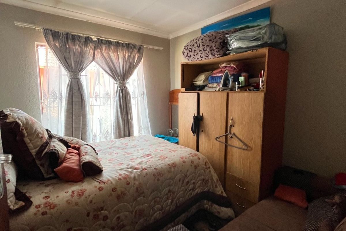 A compact bedroom featuring a window with curtain rods and a ceiling light fixture, requiring some cosmetic updates to the ceiling and walls.