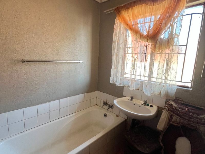 A compact bathroom featuring a bathtub, pedestal basin, and toilet, with tiled splashbacks and security bars on the window.