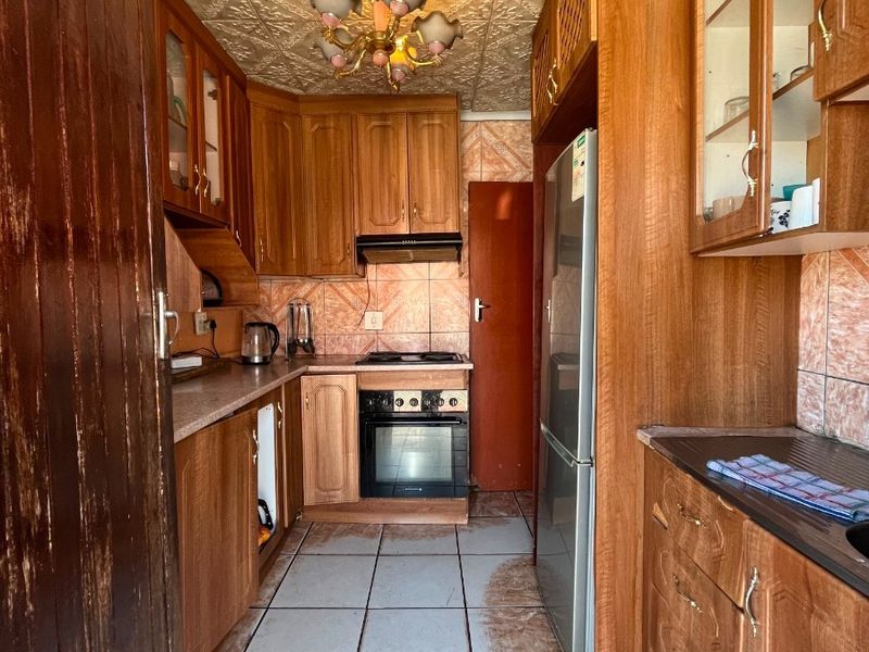 A compact kitchen featuring wooden cabinetry, built-in oven, hob, and extractor fan, with tiled flooring and backsplash throughout.