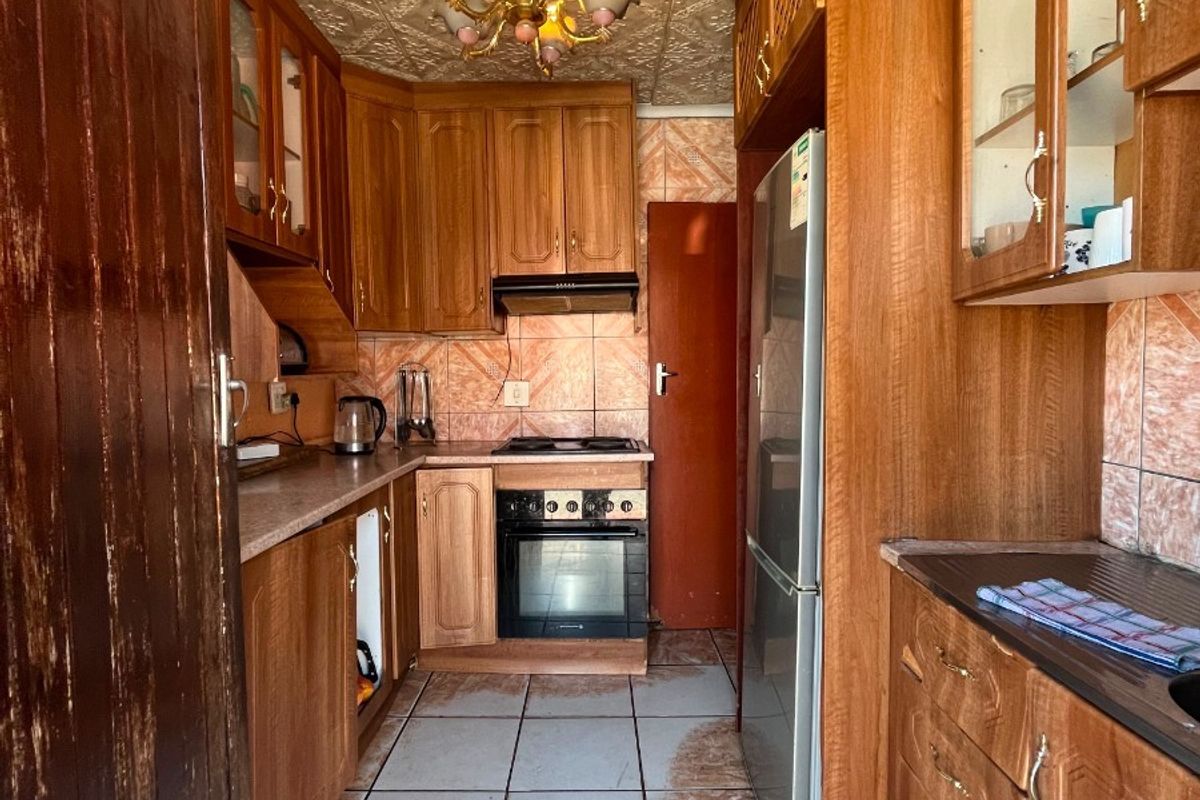 A compact kitchen featuring wooden cabinetry, built-in oven, hob, and extractor fan, with tiled flooring and backsplash throughout.