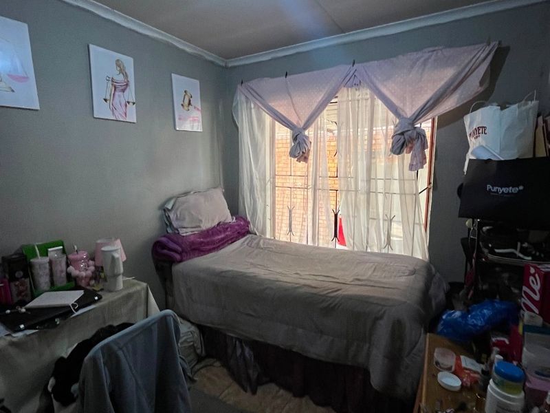 A compact bedroom featuring tiled flooring, a ceiling light fixture, and a security gate on the window.