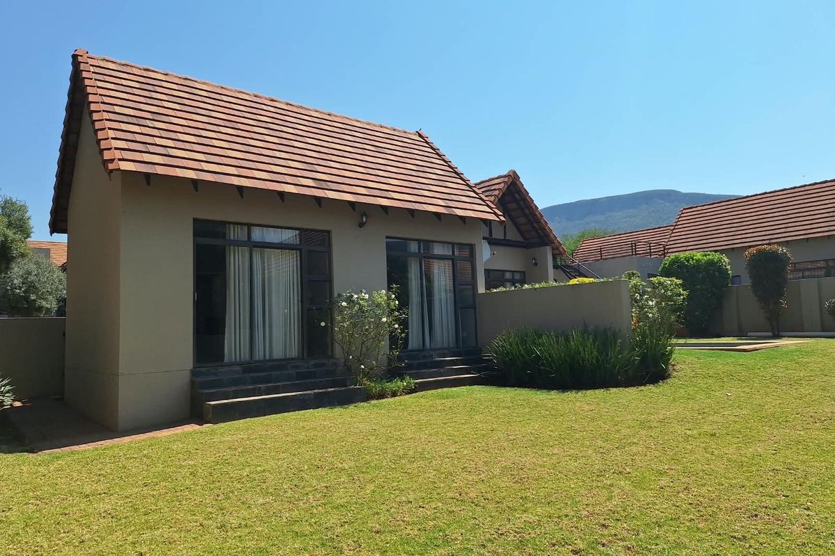 Rear view of a well-maintained residential property featuring a tiled roof, sliding glass doors, and a spacious private lawn area.