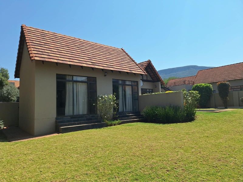 Rear view of a well-maintained residential property featuring a tiled roof, sliding glass doors, and a spacious private lawn area.