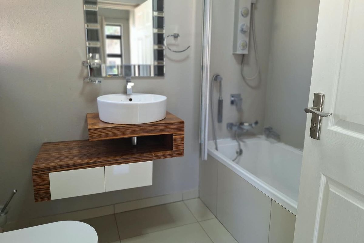 Modern bathroom featuring a floating vanity with a vessel sink, a bathtub with shower mixer, and neutral tiled flooring.
