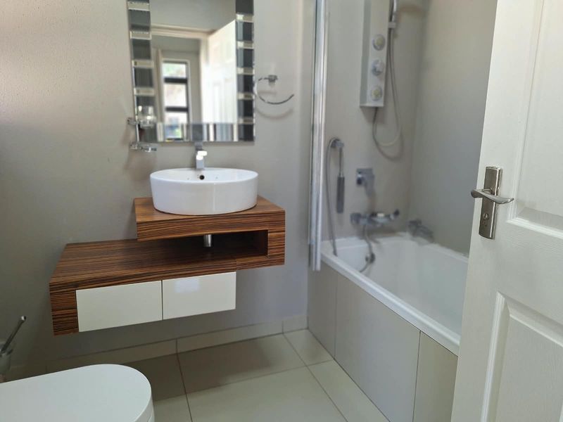 Modern bathroom featuring a floating vanity with a vessel sink, a bathtub with shower mixer, and neutral tiled flooring.
