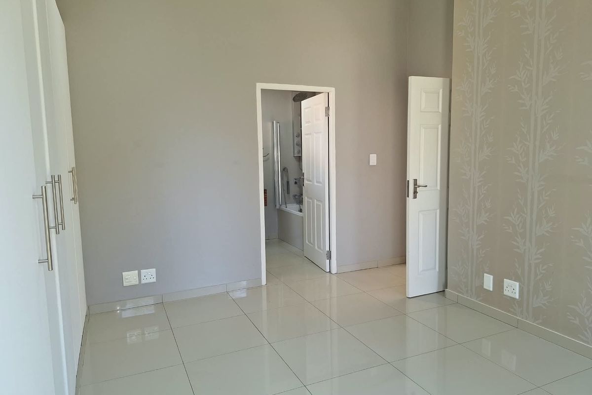 A bright, empty bedroom featuring neutral tiled flooring, built-in cupboards, and direct access to an en-suite bathroom.