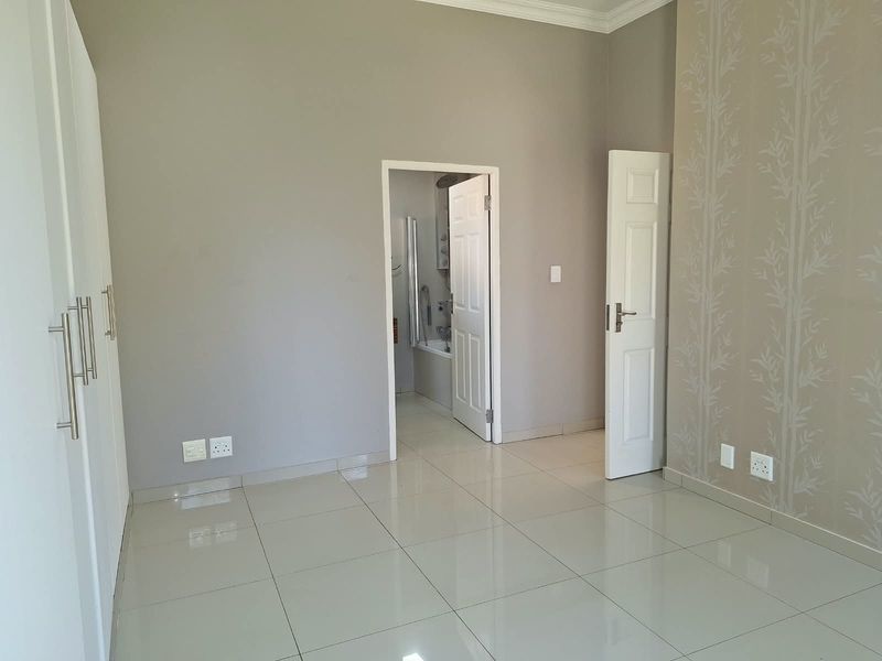 A bright, empty bedroom featuring neutral tiled flooring, built-in cupboards, and direct access to an en-suite bathroom.