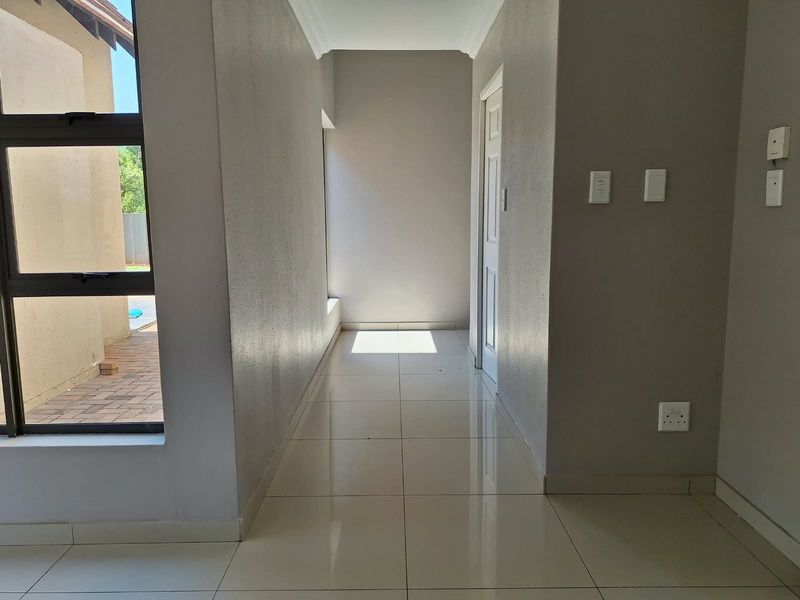 A bright, empty hallway featuring neutral tiled flooring, clean wall finishes, and a large window providing natural light and a view of the exterior.