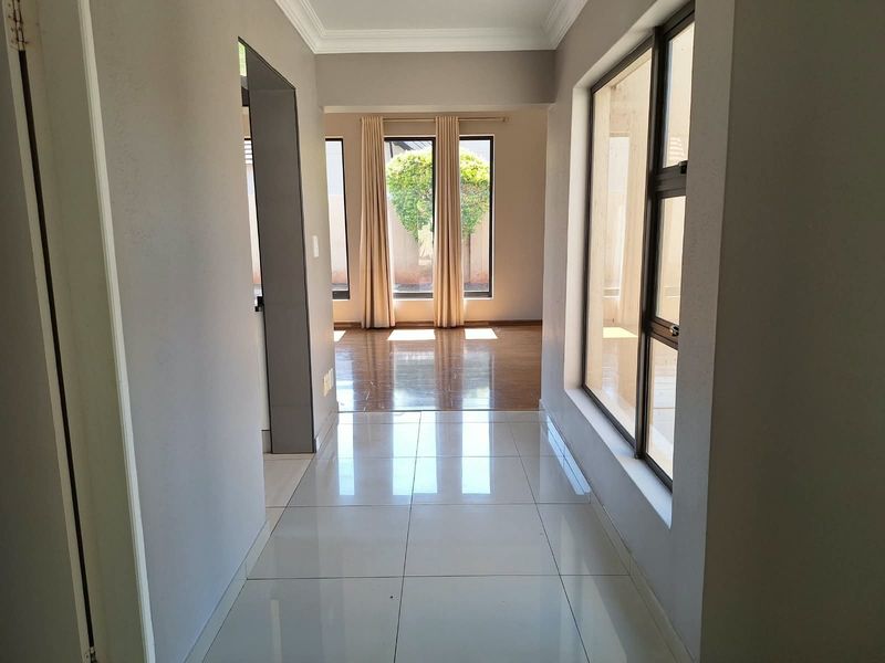 A bright and spacious hallway featuring polished floor tiles, neutral wall tones, and large windows that allow for ample natural light.