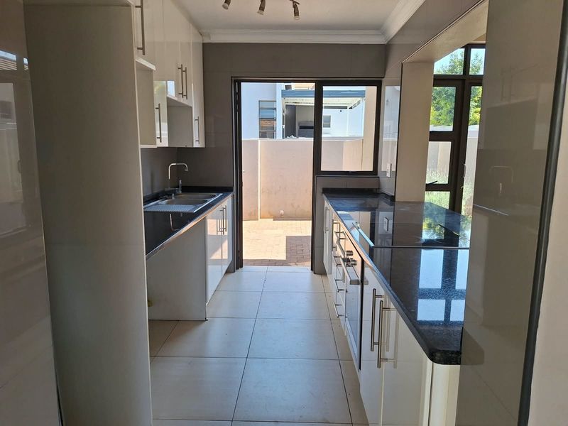 A modern, clean kitchen featuring white cabinetry, dark granite countertops, built-in oven and hob, and direct access to an outdoor patio area.