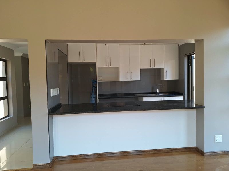 A modern open-plan kitchen featuring white cabinetry, dark granite countertops, an integrated hob, and a breakfast bar overlooking the living area.