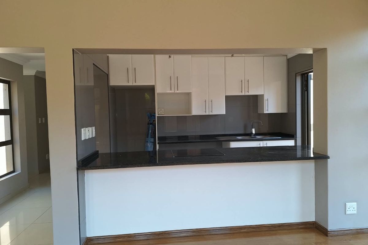 A modern open-plan kitchen featuring white cabinetry, dark granite countertops, an integrated hob, and a breakfast bar overlooking the living area.