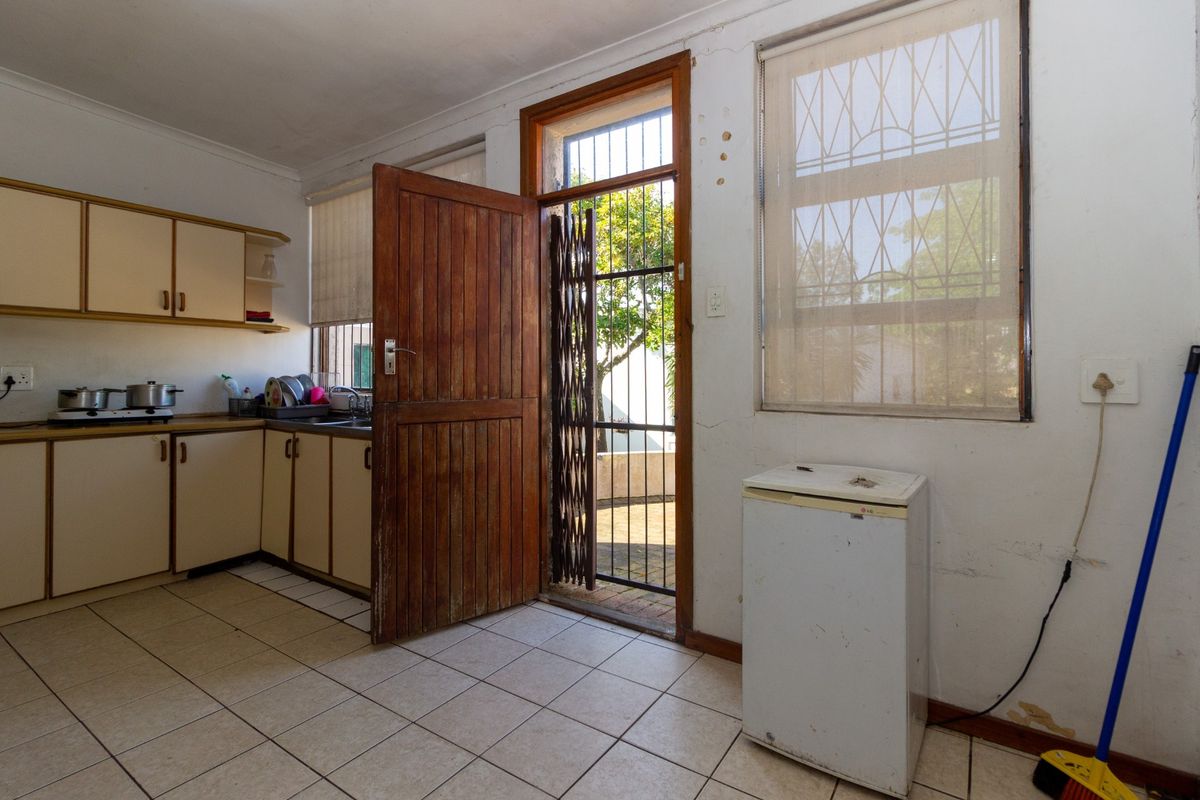 A functional kitchen area featuring built-in cabinetry, tiled flooring, and direct access to an outdoor space through a timber door with a security gate.