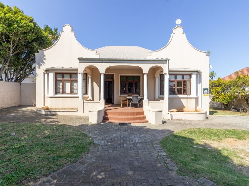 Front elevation of a classic Cape Dutch style office building featuring a covered porch, paved driveway, and established garden surroundings.