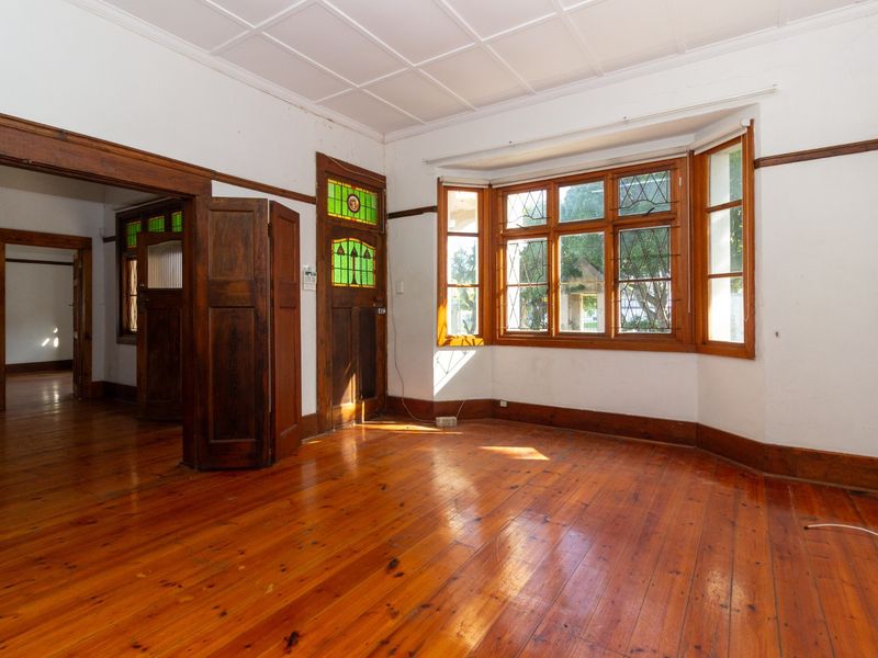 Spacious office area featuring polished timber flooring, a large bay window with leaded glass, and classic timber door frames with stained glass accents.