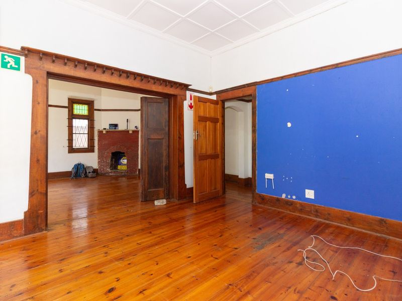 Spacious office area featuring original hardwood flooring, ornate timber door frames, and a classic brick fireplace, offering a character-filled workspace.