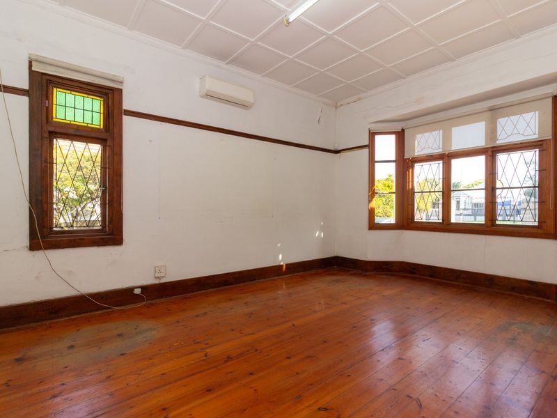 An empty office space featuring original timber flooring, a bay window with stained glass accents, and a coffered ceiling.